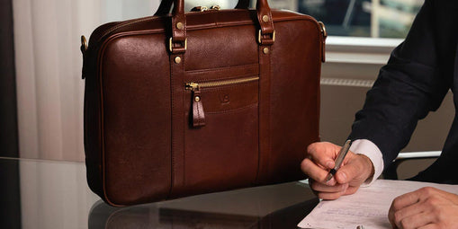 man signing a document next to a leather briefcase on a table