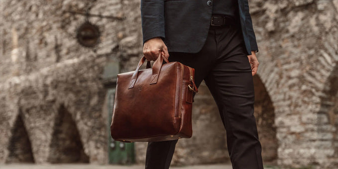 man in a suit holding a brown leather laptop bag