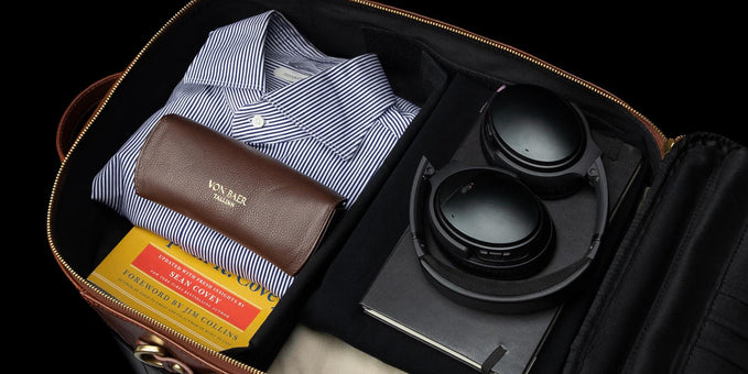 Interior view of a brown leather travel bag organized with clothes, headphones, and a book.