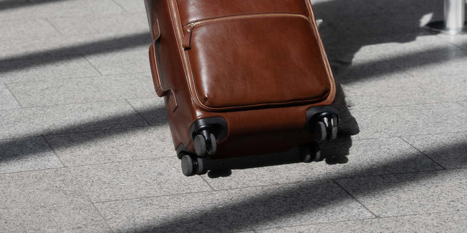 Woman pulling a brown leather carry-on suitcase and matching laptop bag in an airport terminal.