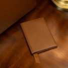 Leather passport holder on a vintage table near an old lamp and a luxury tote bag
