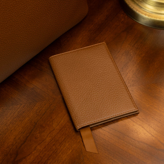 Leather passport holder on a vintage table near an old lamp and a luxury tote bag