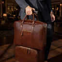 Von Baer City large full-grain leather laptop bag in brown on a trolley suitcase in a luxury hotel lobby, premium business travel bag.