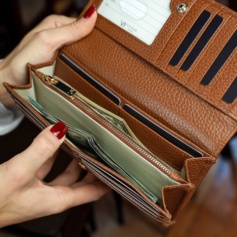 Von Baer Allure large cognac tan full-grain leather accordion wallet held by a woman, showing two cash compartments filled with dollar bills.