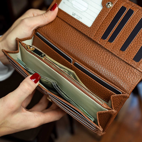 Von Baer Allure large cognac tan full-grain leather accordion wallet held by a woman, showing two cash compartments filled with dollar bills.