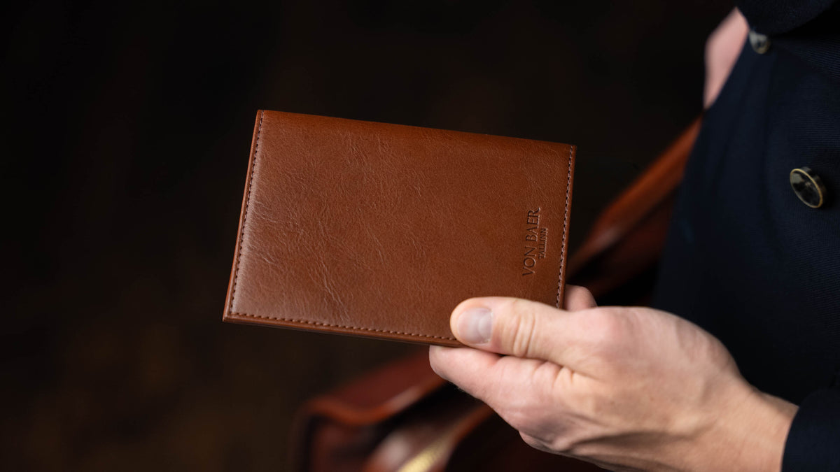 Von Baer Atlas full grain leather passport holder held by a gentleman in a navy blue suit on black background