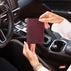 A person holding a luxury von baer burgundy pebbled leather passport holder / small document case inside a car, with the steering wheel and dashboard visible in the background.