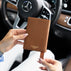 A woman holds a brown textured luxurious leather passport cover with a gold-tone Von Baer logo in a Mercedes car interior. The background shows a Mercedes-Benz steering wheel and dashboard.