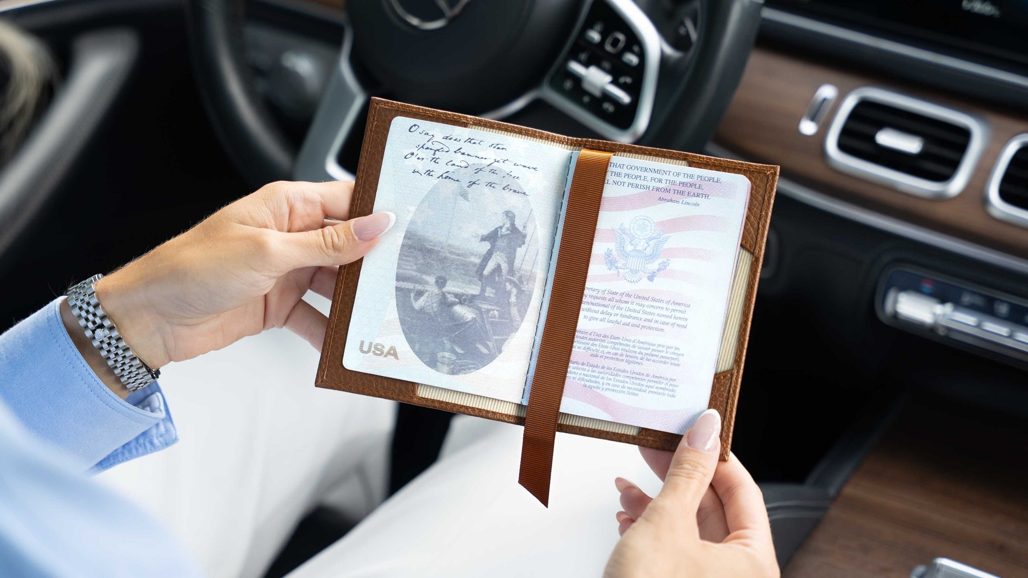 A person holding an open brown von baer leather passport holder / document case inside a car, showing a USA passport