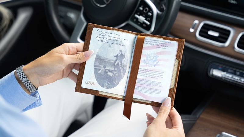 A person holding an open brown von baer leather passport holder / document case inside a car, showing a USA passport