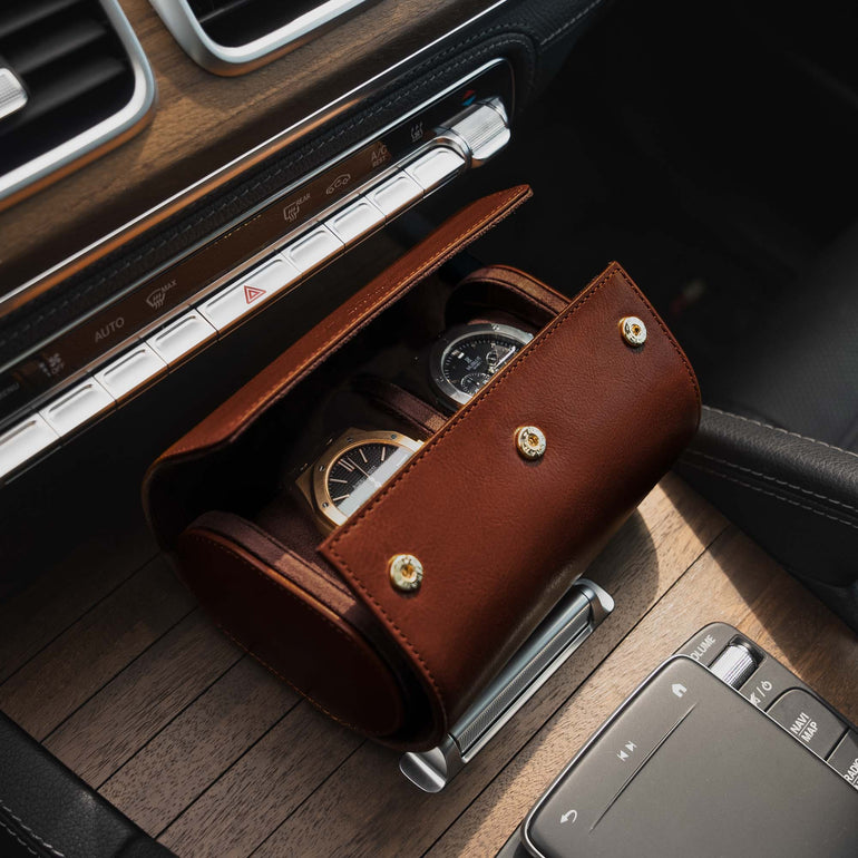 A brown Von Baer Calibre luxury full-grain leather watch roll case with two slots, opened with watches inside, in a Mercedes car.