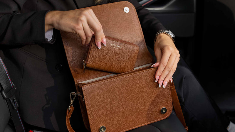 Von Baer Celeste luxury cognac tan leather wallet shown inside an open Isabella small crossbody bag, held by a person in a black blazer inside a car interior.
