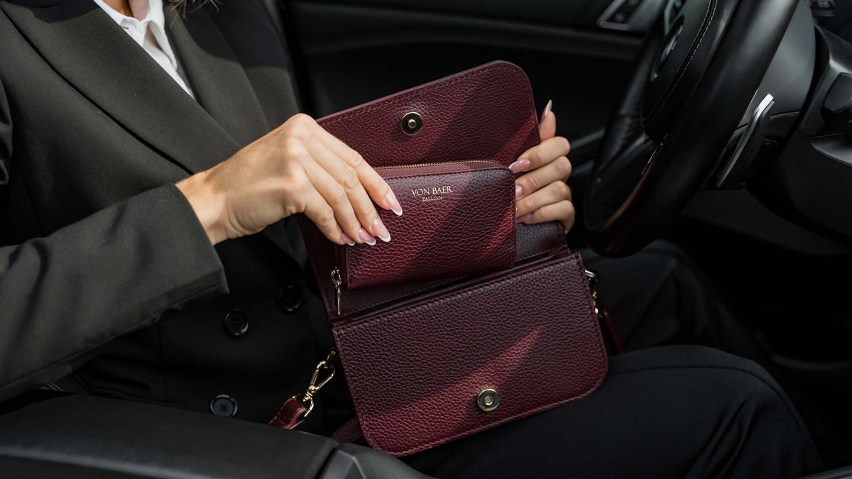 Von Baer Celeste burgundy premium full-grain leather wallet shown open inside an Isabella small leather crossbody bag setting, held by a person inside a car interior to display fit and layout.