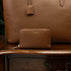 Von Baer Celeste small luxury compact tan leather zip-around wallet, displayed on a vintage wooden table next to a leather tote bag.