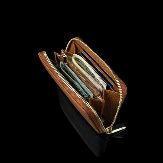 Von Baer Celeste small tan full-grain leather zip-around wallet shown filled with cards and dollar notes, featuring RFID protection, gold-tone zipper hardware, and gold-embossed Von Baer Tallinn branding against a black background.