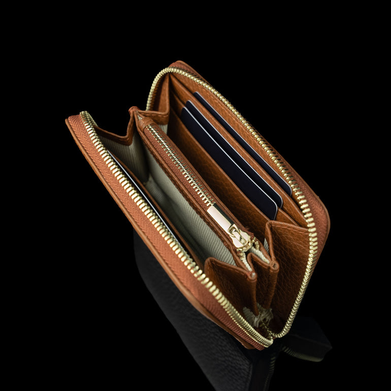 Von Baer Celeste small tan full-grain leather zip-around wallet shown filled with cards, featuring RFID protection, gold-tone zipper hardware, and gold-embossed Von Baer Tallinn branding against a black background.