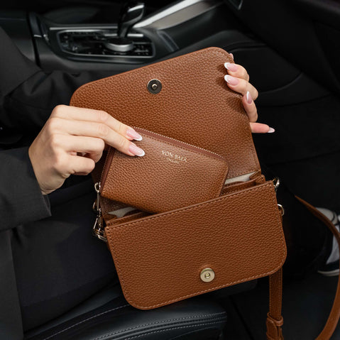 Von Baer Isabella small cognac leather crossbody bag and Celeste women's compact leather purse shown in an everyday essentials set inside a car interior.