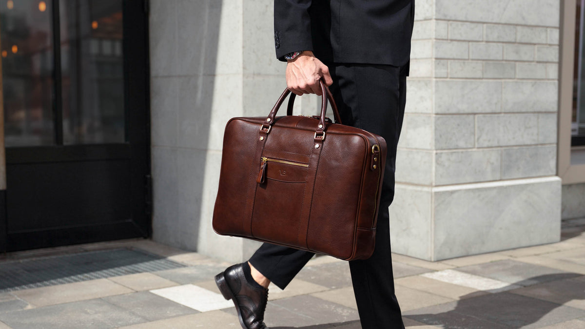Von Baer City large men's brown leather laptop bag, held by a person in a business outfit in an urban financial district setting