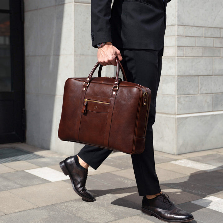 Von Baer City large men's brown leather laptop bag, held by a person in business attire in an urban financial district setting