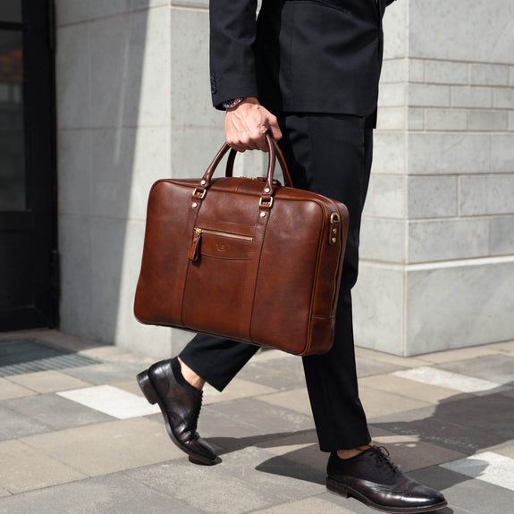 Von Baer City large men's brown leather laptop bag, held by a person in business attire in an urban financial district setting