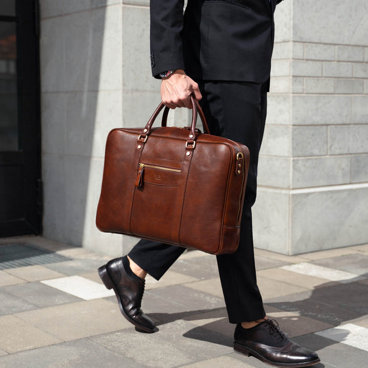 Von Baer City large men's brown leather laptop bag, held by a person in business attire in an urban financial district setting