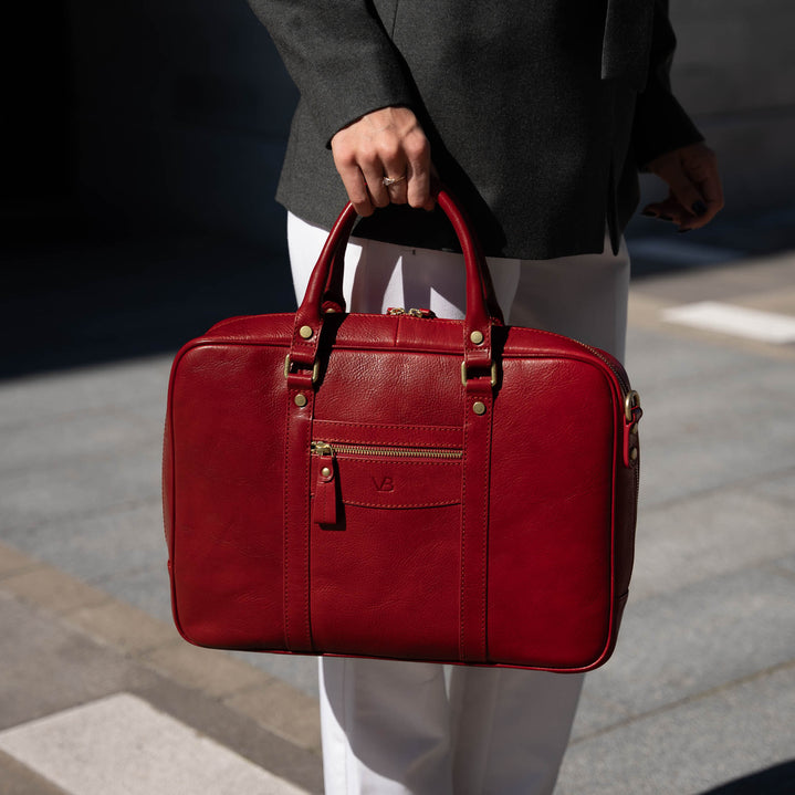 A close-up of a beautiful woman holding a red Von Baer City luxury leather laptop bag with a shoulder strap.