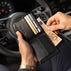 Von Baer Classic bifold leather wallet in black, stuffed with cash and credit cards, shown with a man taking out euro banknotes inside a Porsche