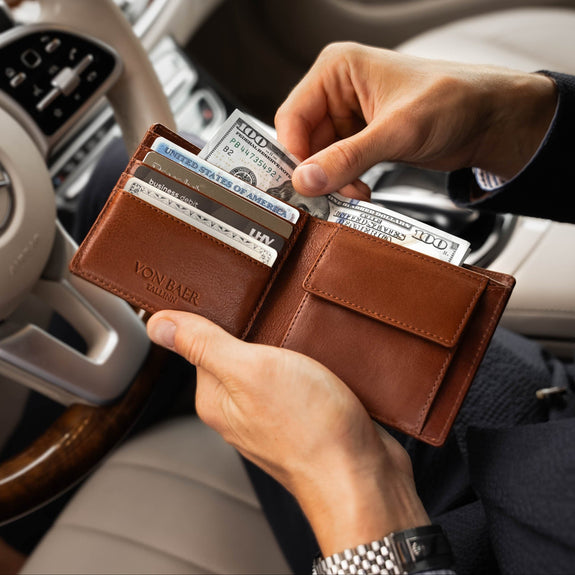 Von Baer Classic bifold leather wallet in brown, stuffed with cash and credit cards like American Express, shown with a man taking out dollars in a Porsche interior