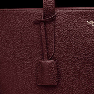 Von Baer decorative leather clip with snap hook in burgundy color on tote bag, front view showing premium hardware detail.