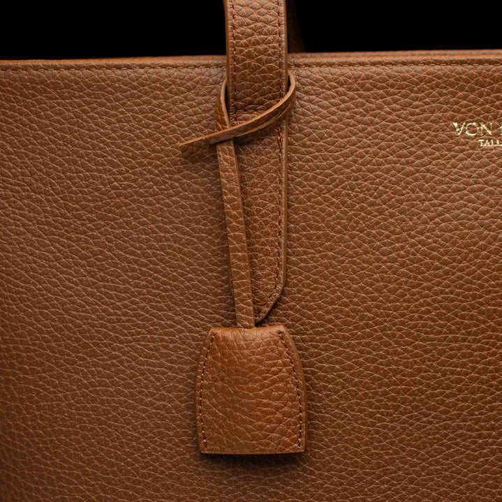 Von Baer decorative leather clip with snap hook in cognac tan color on tote bag, front view showing premium hardware detail.