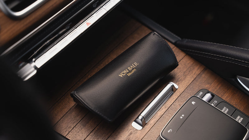 A rear-side view of a black Von Baer Deluxe luxury leather sunglasses and glasses case on a wooden panel in a car.