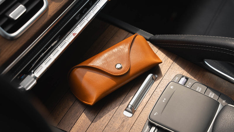 A front-side view of a tan Von Baer Deluxe luxury leather sunglasses and glasses case on a wooden panel in a car.