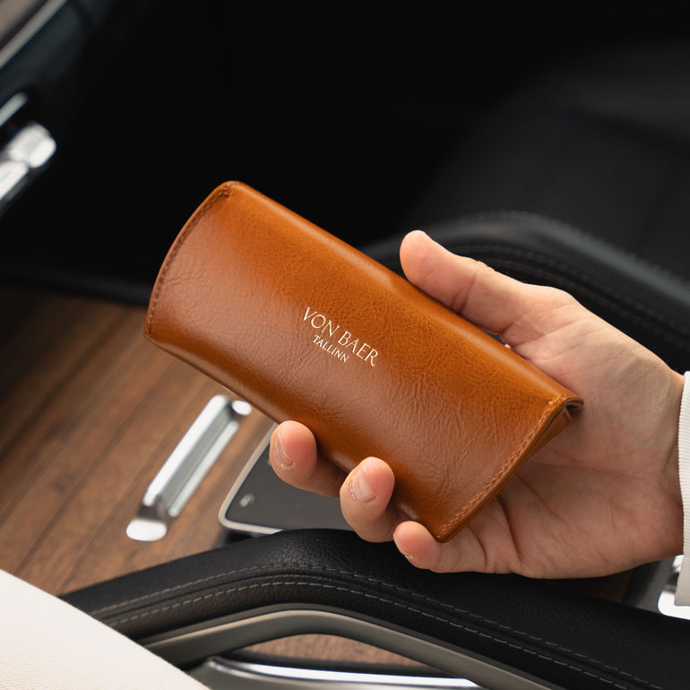 Hand holding a tan leather wallet with 'Von Baer' branding inside a car.