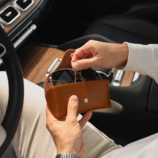Person holding a high quality tan leather sunglasses case with sunglasses inside, sitting in a car.