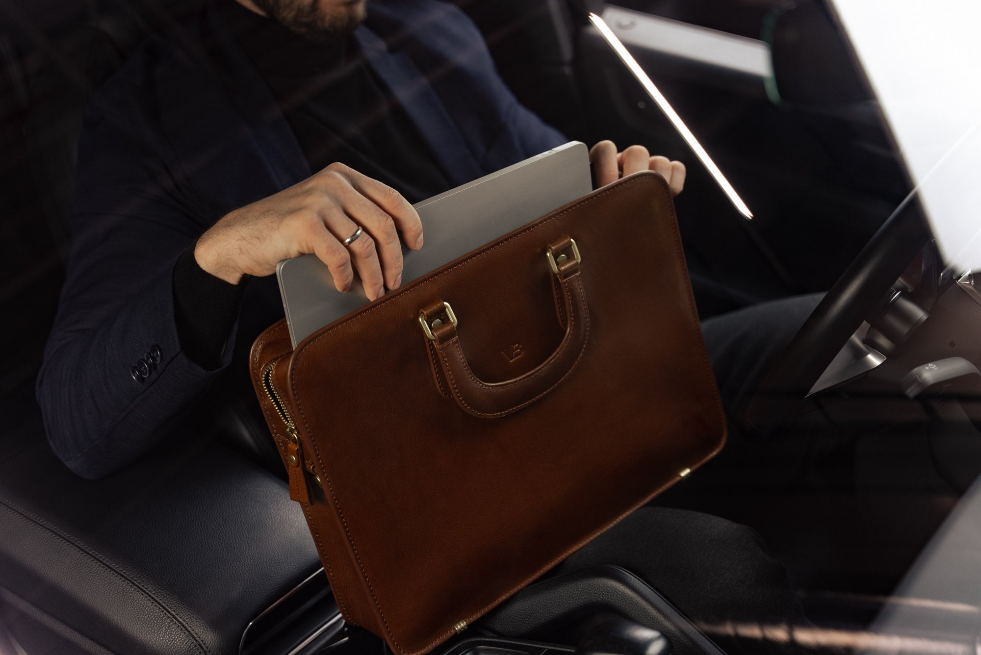 A businessman taking a MacBook out of a Von Baer elegant luxury slim full-grain leather laptop bag inside a Porsche car.