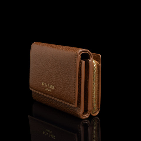 Von Baer Elise women's cognac pebbled leather trifold wallet shown from a side view on a reflective black background, highlighting its gold zipper hardware and gold-embossed Von Baer Tallinn logo.