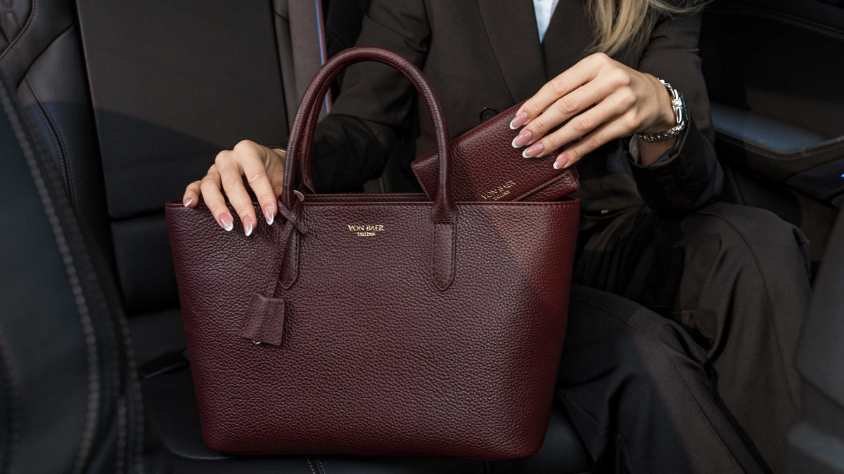 Von Baer Elise cognac tan leather trifold wallet for women shown with an Isabella small leather crossbody bag, held by a woman in a black blazer inside a car interior displaying storage details.