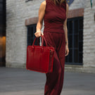 A woman walking in a city, holding a red Von Baer exquisite luxury leather laptop bag.