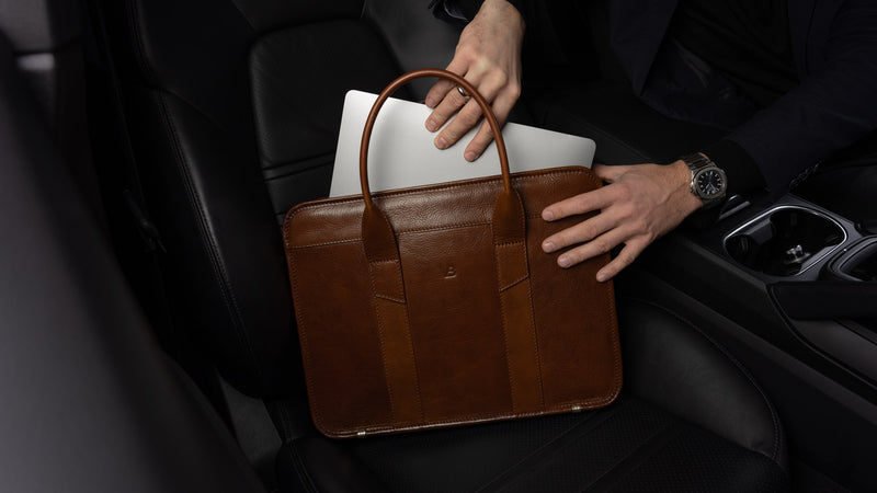 A businessman taking a MacBook out of a Von Baer exquisite luxury slim full-grain leather laptop bag inside a Porsche car.