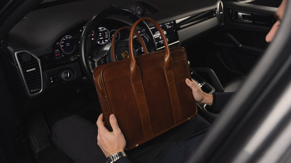 A man's hand holding a Von Baer exquisite luxury slim full-grain leather laptop bag inside a Porsche car.