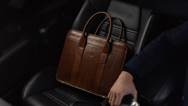 A Von Baer exquisite luxury slim full-grain leather laptop bag is shown inside a Porsche, near a male model.