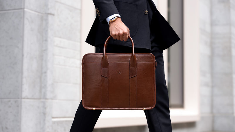 An exquisite, slim, brown Von Baer full-grain leather laptop briefcase held by a man in a suit