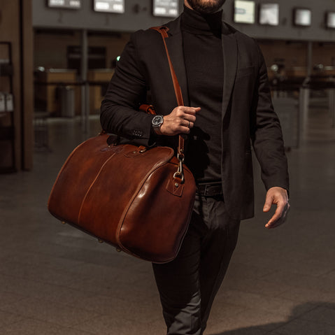 Grand leather garment bag in brown carried by man in black suit in an airport