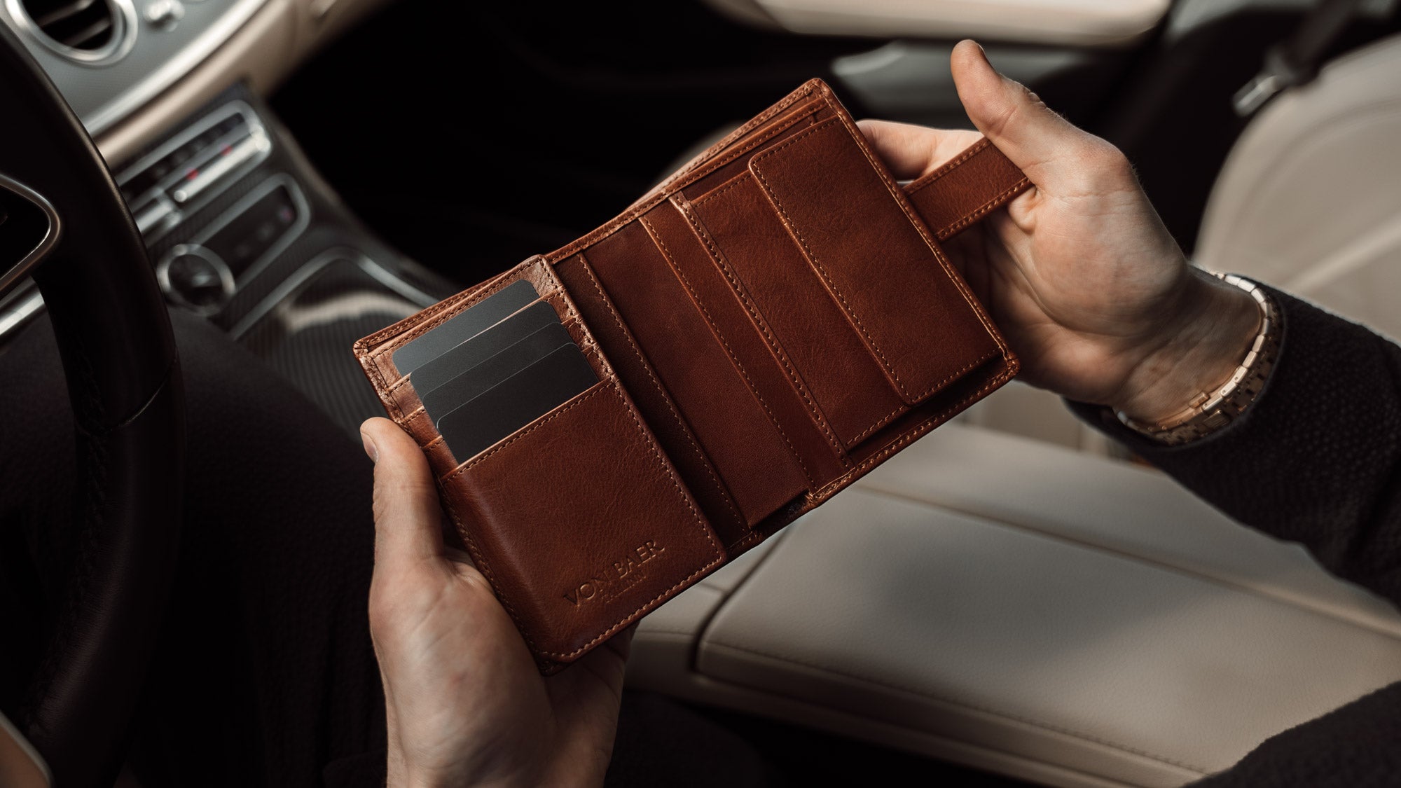 Von Baer Heritage premium men's leather trifold wallet in solid brown, opened in the car, slider.