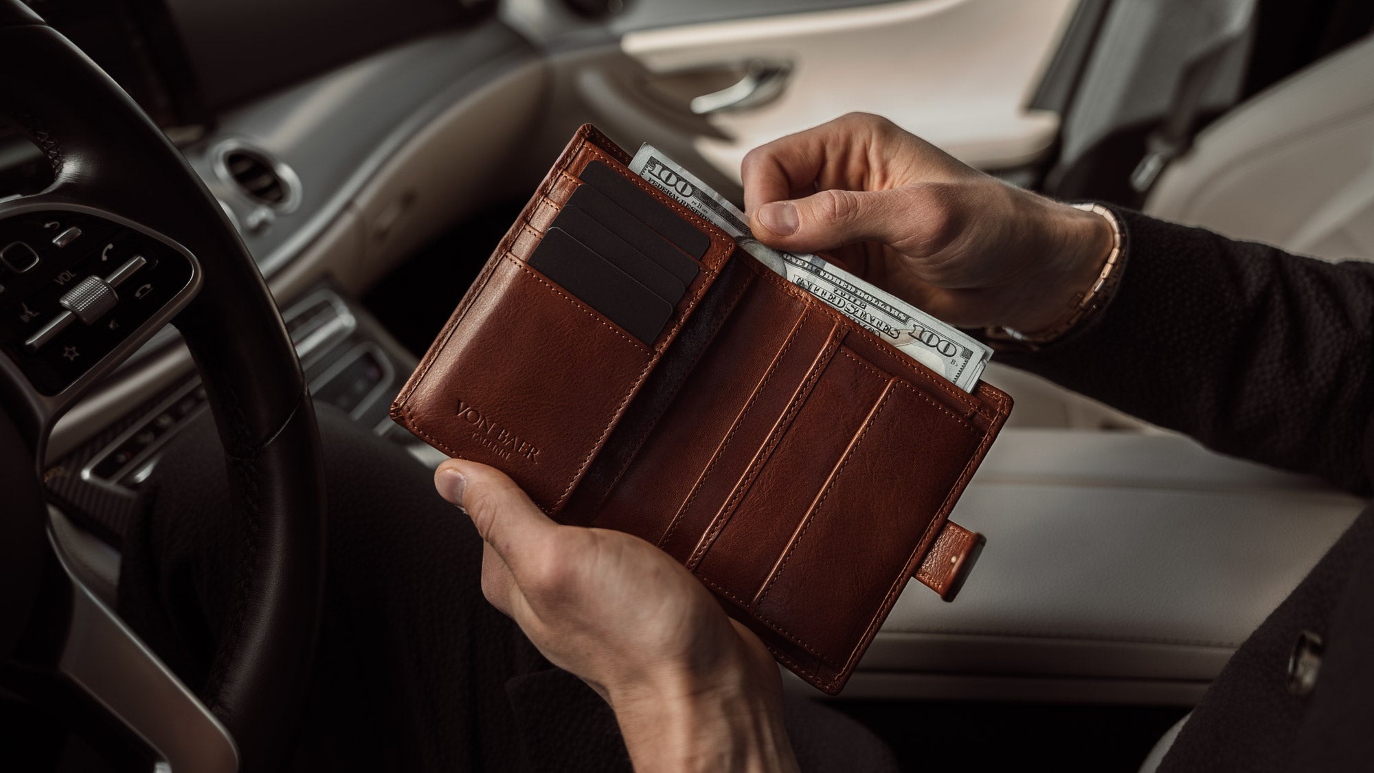 Von Baer Heritage premium men's leather trifold wallet in solid brown, with cash in the car, slider.