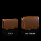 Von Baer Isabella and Isabella Grande women's full-grain pebbled leather crossbody bags in cognac and tan, displayed side by side on a reflective black background to compare sizes, with the smaller Isabella bag on the left and the larger Isabella Grande bag on the right