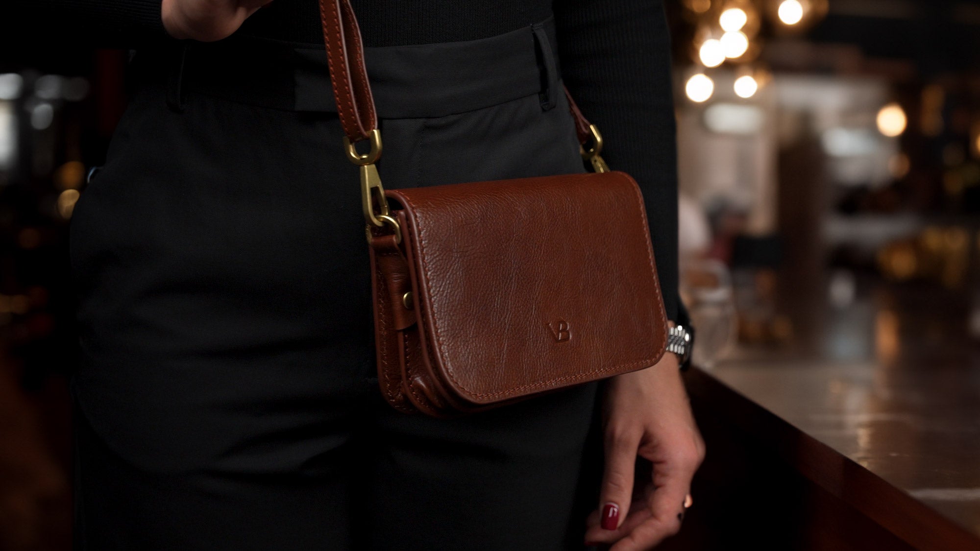 Von Baer Isabella luxury mini leather crossbody bag with adjustable strap in brown, worn by a female model in a café, slider view.