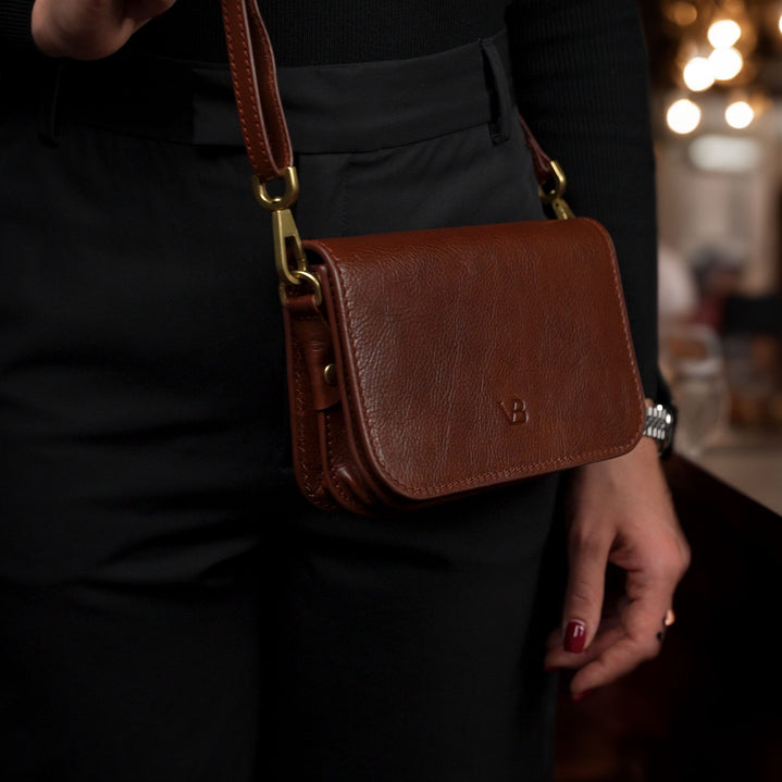 Von Baer Isabella luxury mini leather crossbody bag with adjustable strap in brown, worn by a female model in a café.