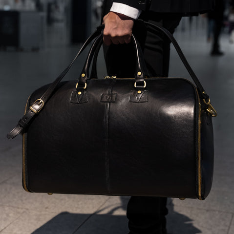 man holding the grand in black by the top handles and shoulder strap