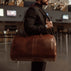 grand leather garment bag in brown shown from the side carried by a man